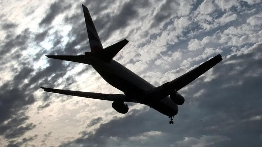 A silhouette of an airplane landing against the dark sky.