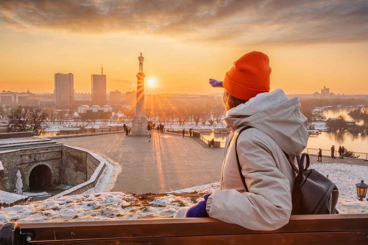 Person seated with a backpack, overlooking a city skyline and river at sunset.