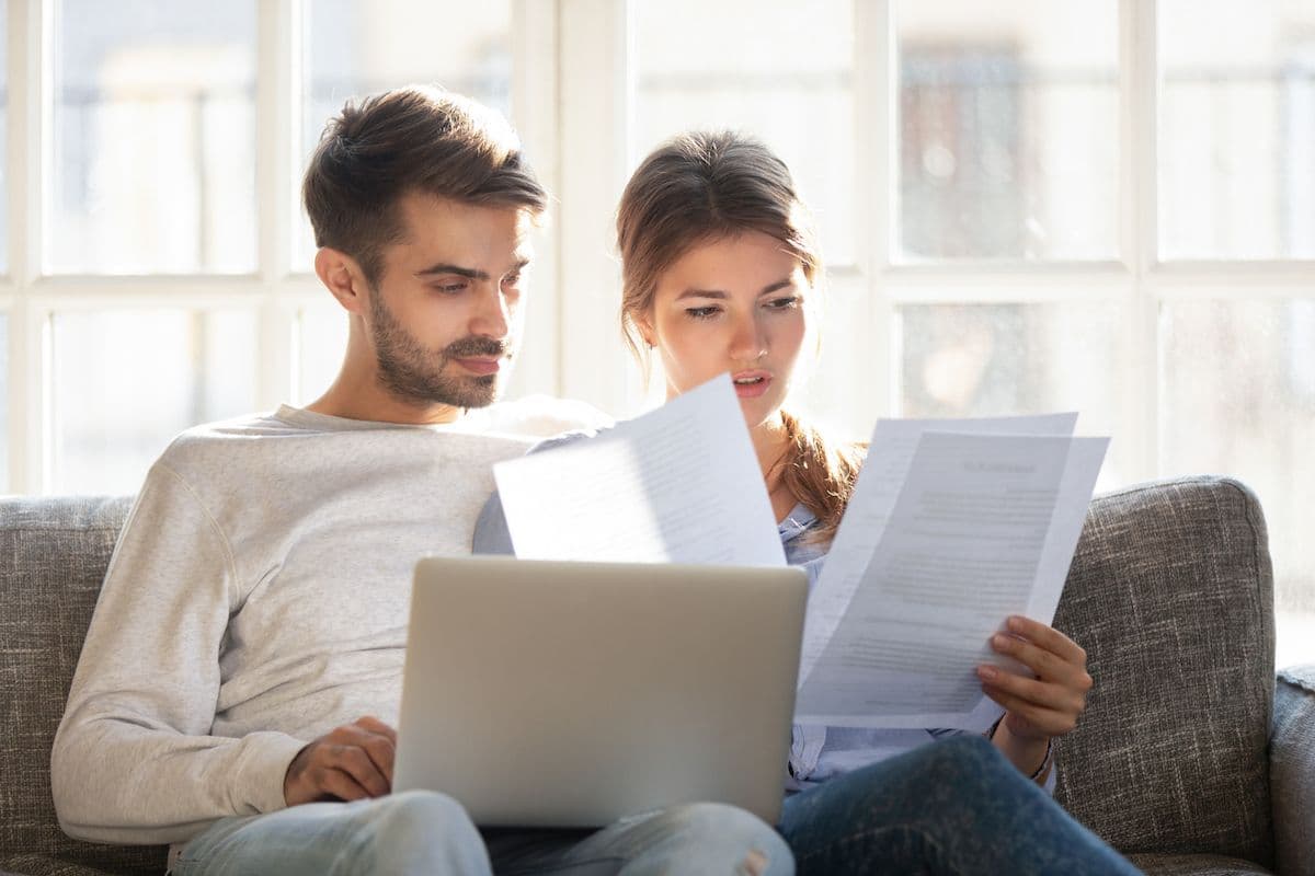 Couple reviewing paperwork and a laptop while sitting on a couch at home.