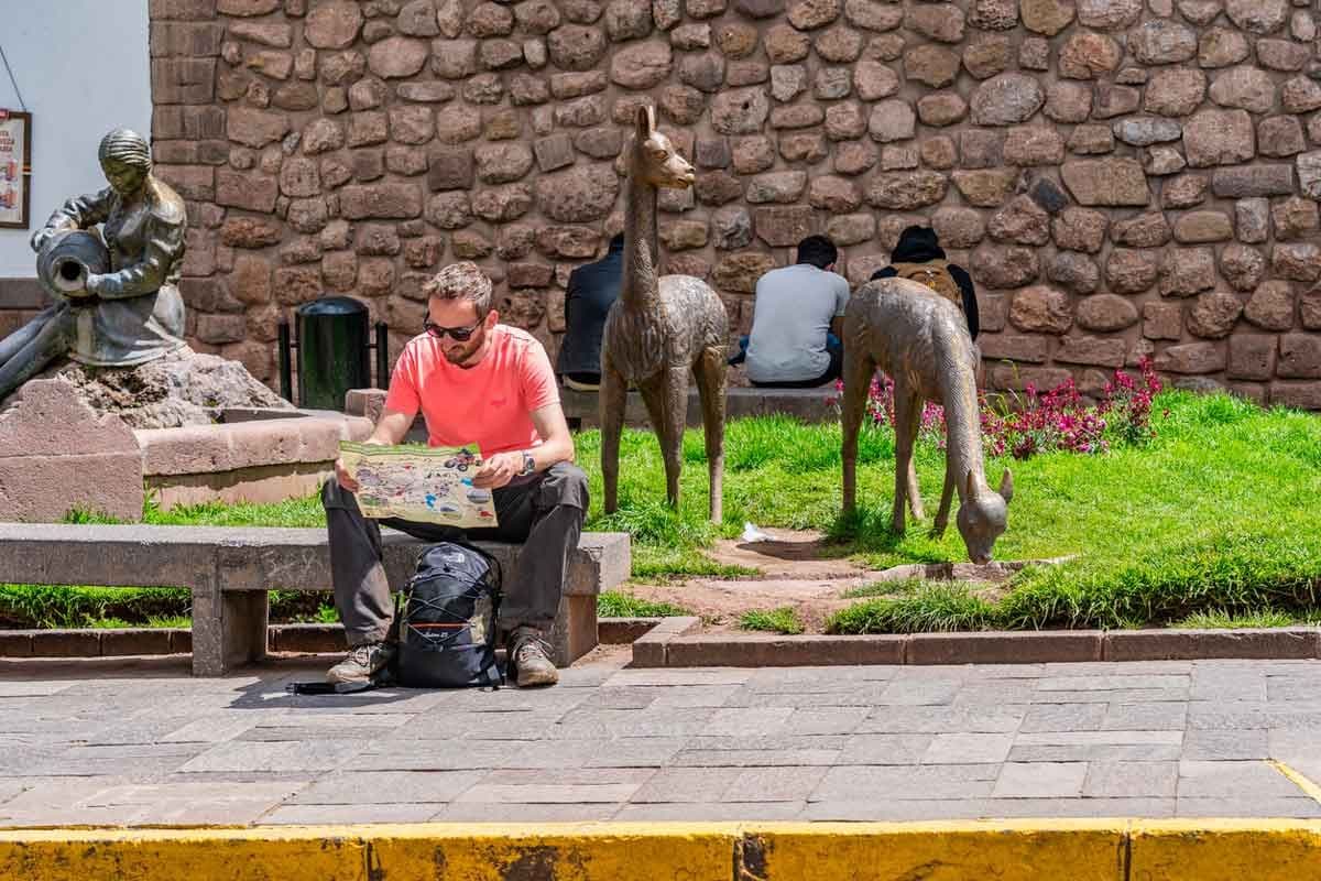 A male traveler sits on a bench looking at a map in Cusco, Peru.