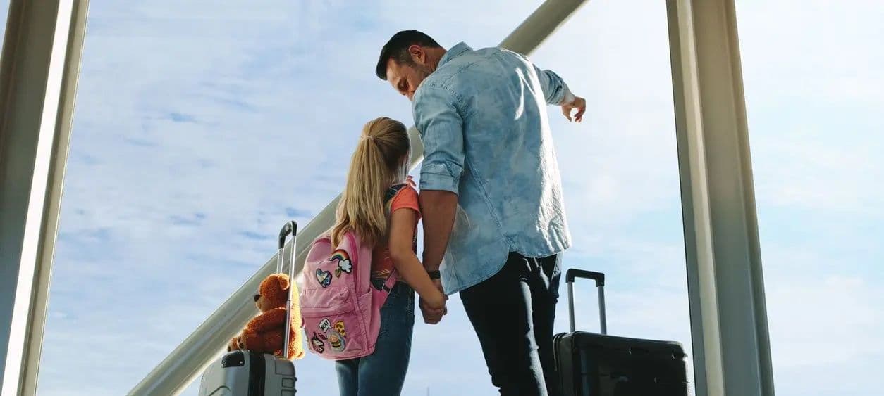 A father and daughter standing together with luggage at an airport