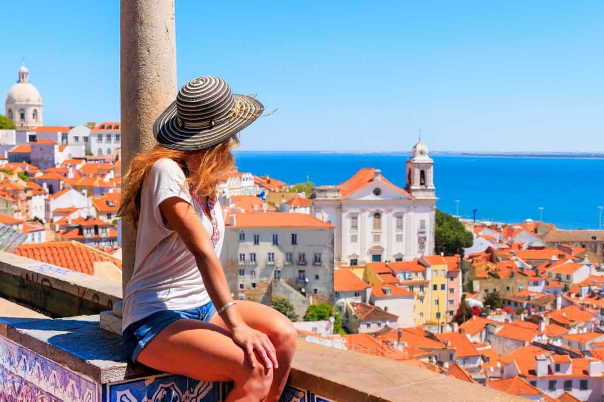 A female tourist sits on a balcony looking out at Lisbon, Portugal.