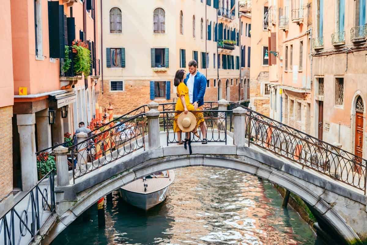 A couple stands on a bridge over a canal in Venice, Italy.