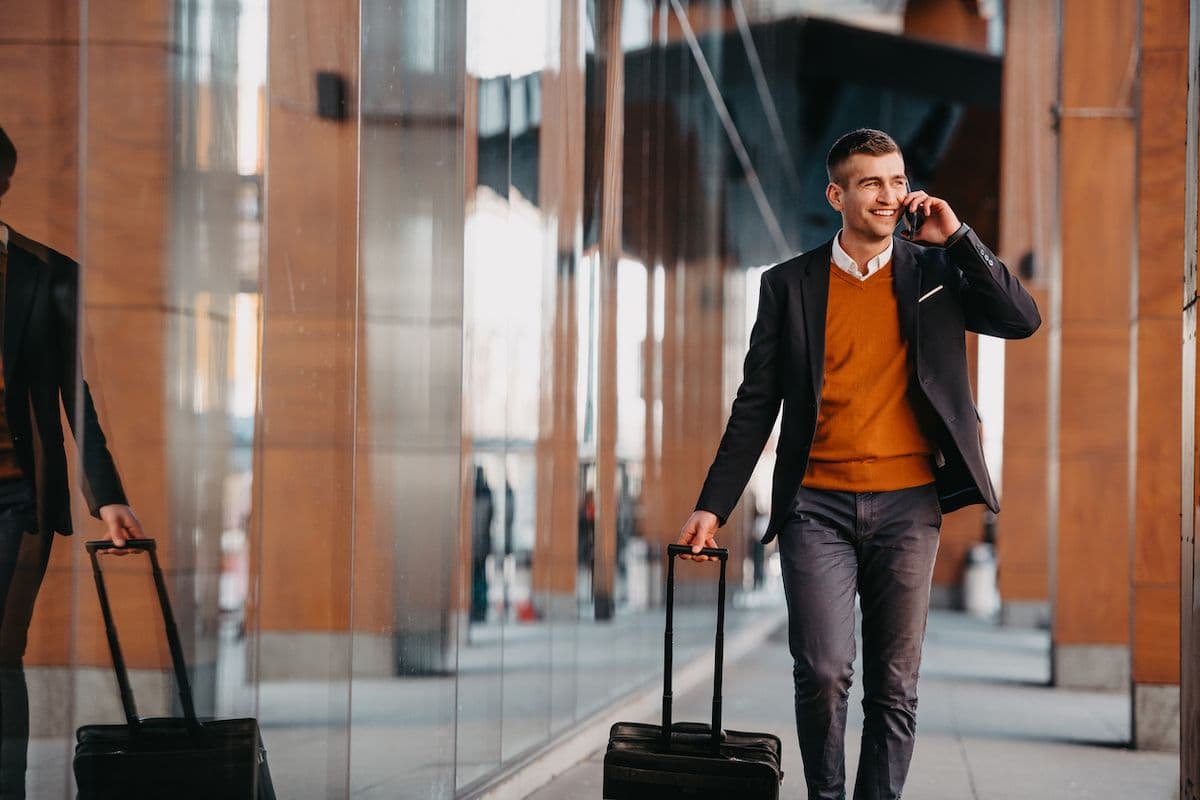 A business traveler rolls his luggage while talking on the phone and walking through a hotel lobby.