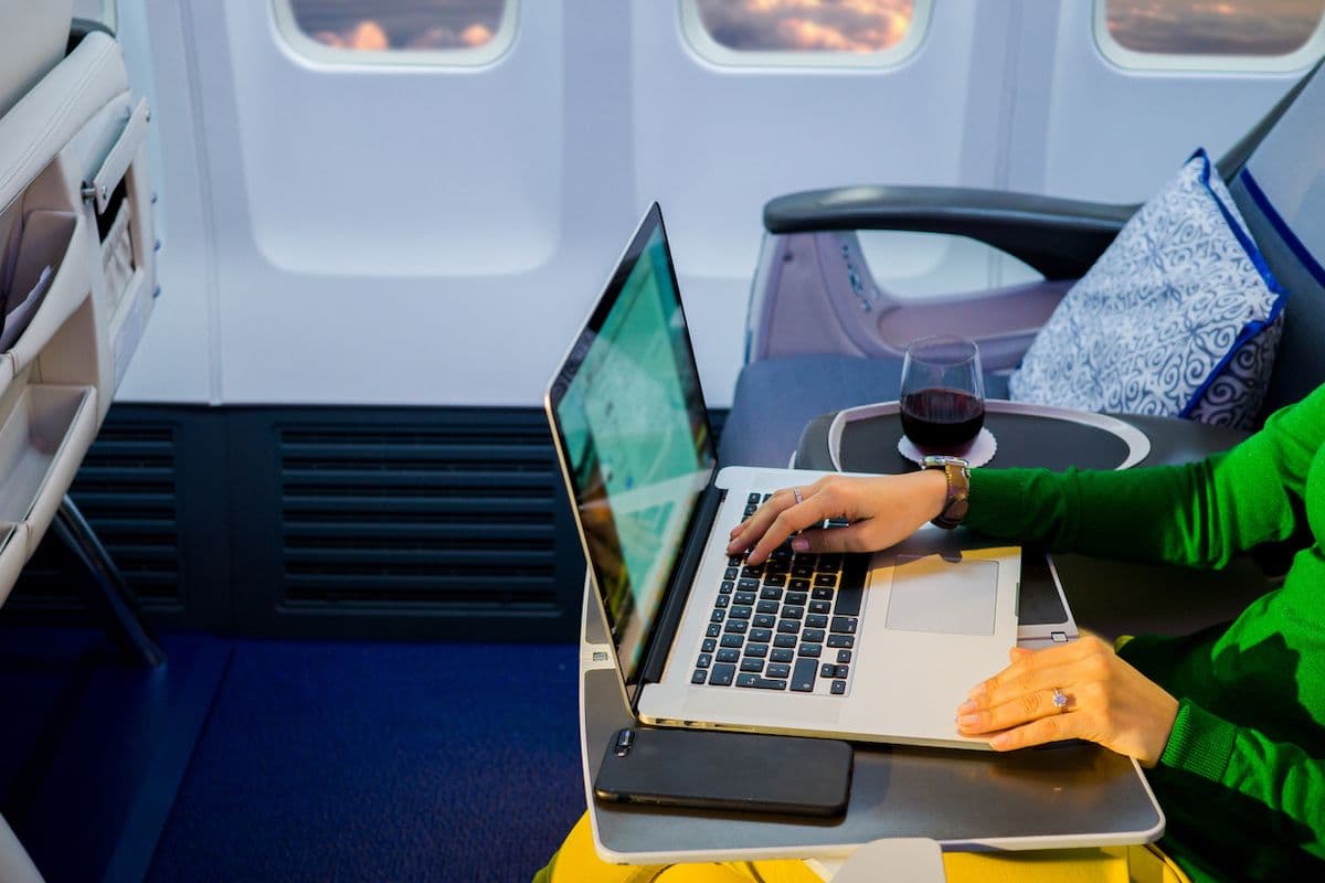 Passenger using a laptop at a tray table on an airplane.