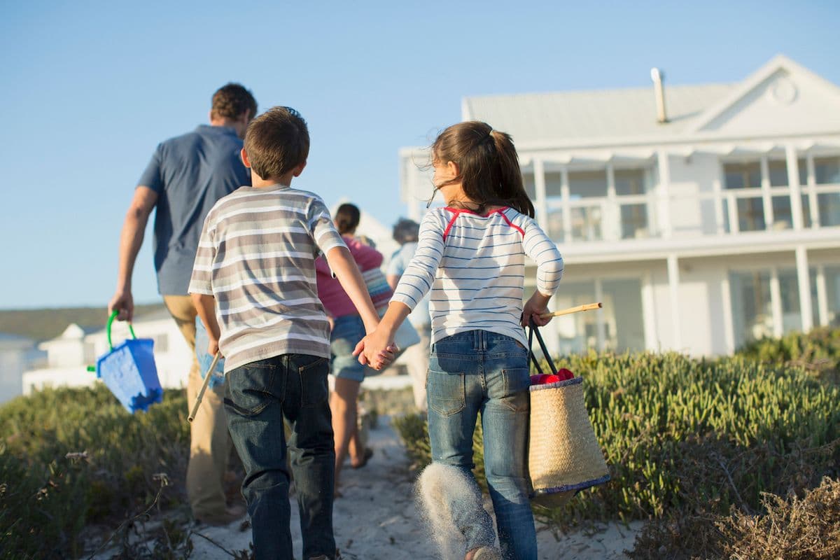 Family walking a sand path toward a white beach house