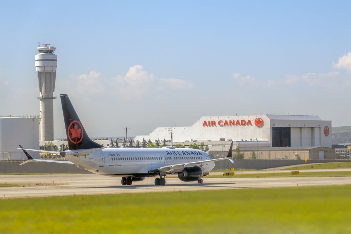 Air Canada jet taxiing past a control tower and hangar at a sunny airport