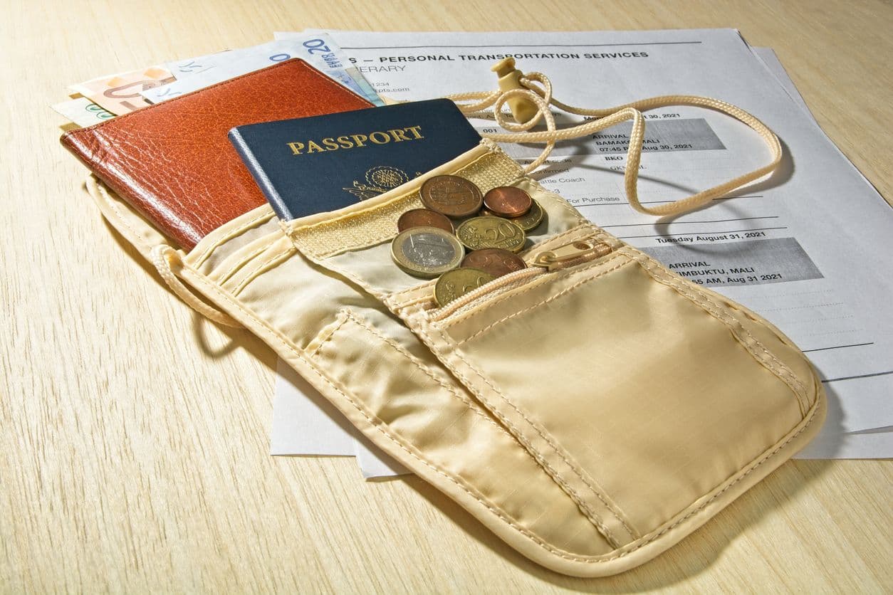 A Boxiki belt bag with on a table packed with a passport, a slim wallet, and coins and foreign currency.