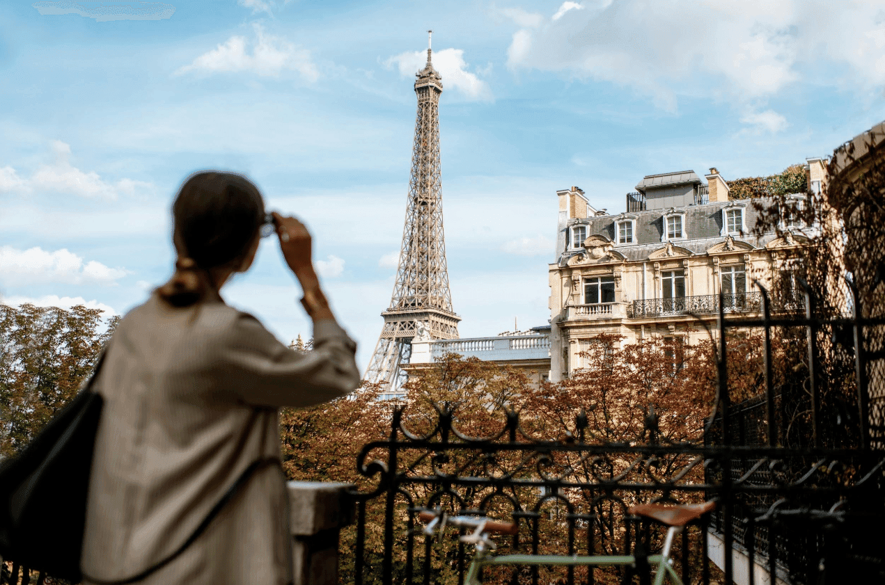 A traveler looks out at the Eiffel Tower and Parisian rooftops from a balcony.