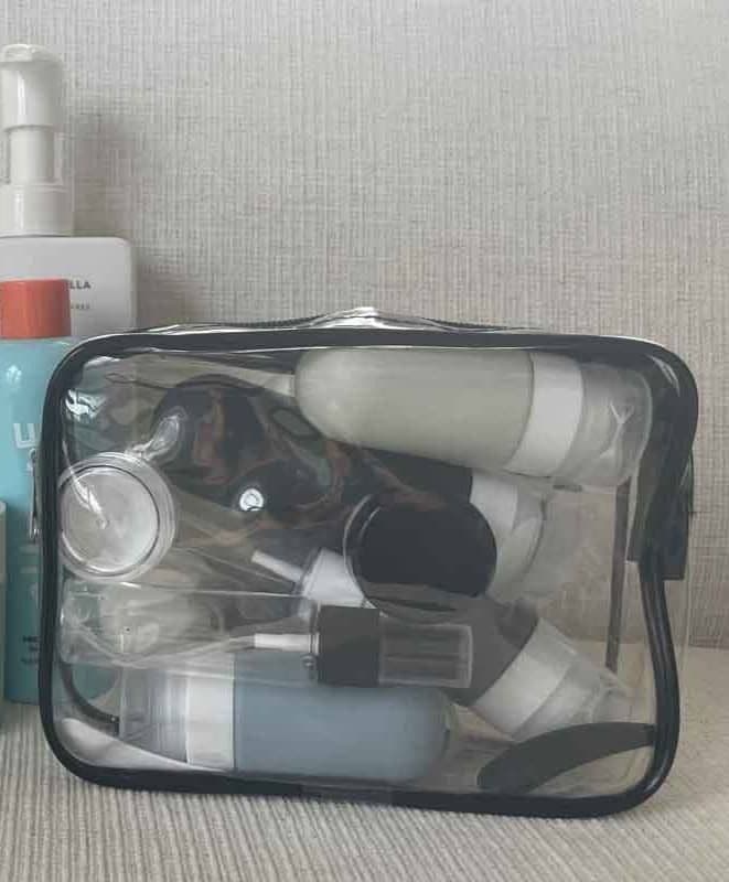 Travel bottles in a clear pouch sitting on a sofa next to various toiletries.