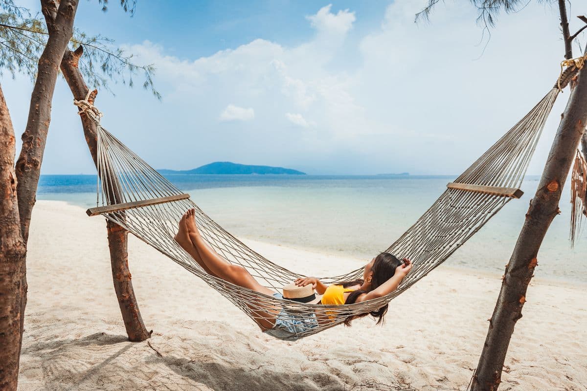 Woman relaxing in a hammock on a quiet beach in Koh Samui, Thailand, with turquoise water and a distant island in the background.