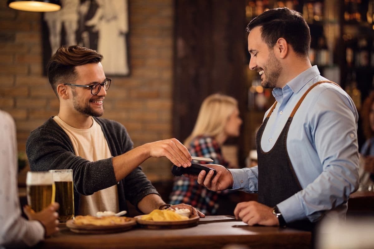 A man eating at a restaurant taps his card to pay while the server holds a card reader.