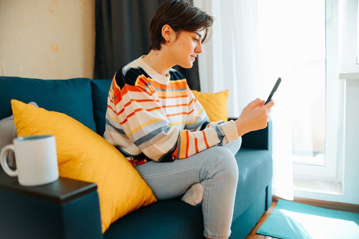 Person sitting on a couch checking their phone at home