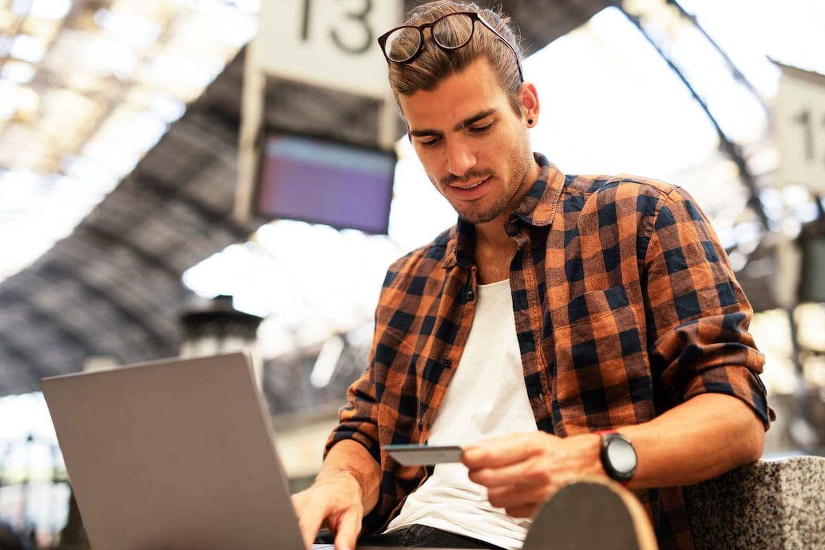 A man holding a credit card while using a laptop at a train station.