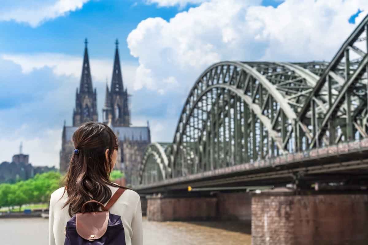 A young woman tourist looking across the Rhine river at the cathedral in Cologne, Germany.