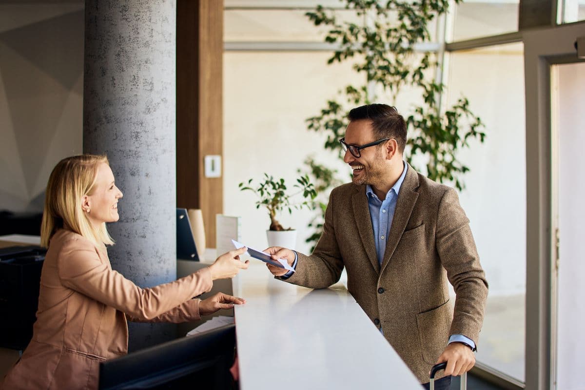 Business traveler at a hotel front desk handing a credit card to a receptionist during check-in.