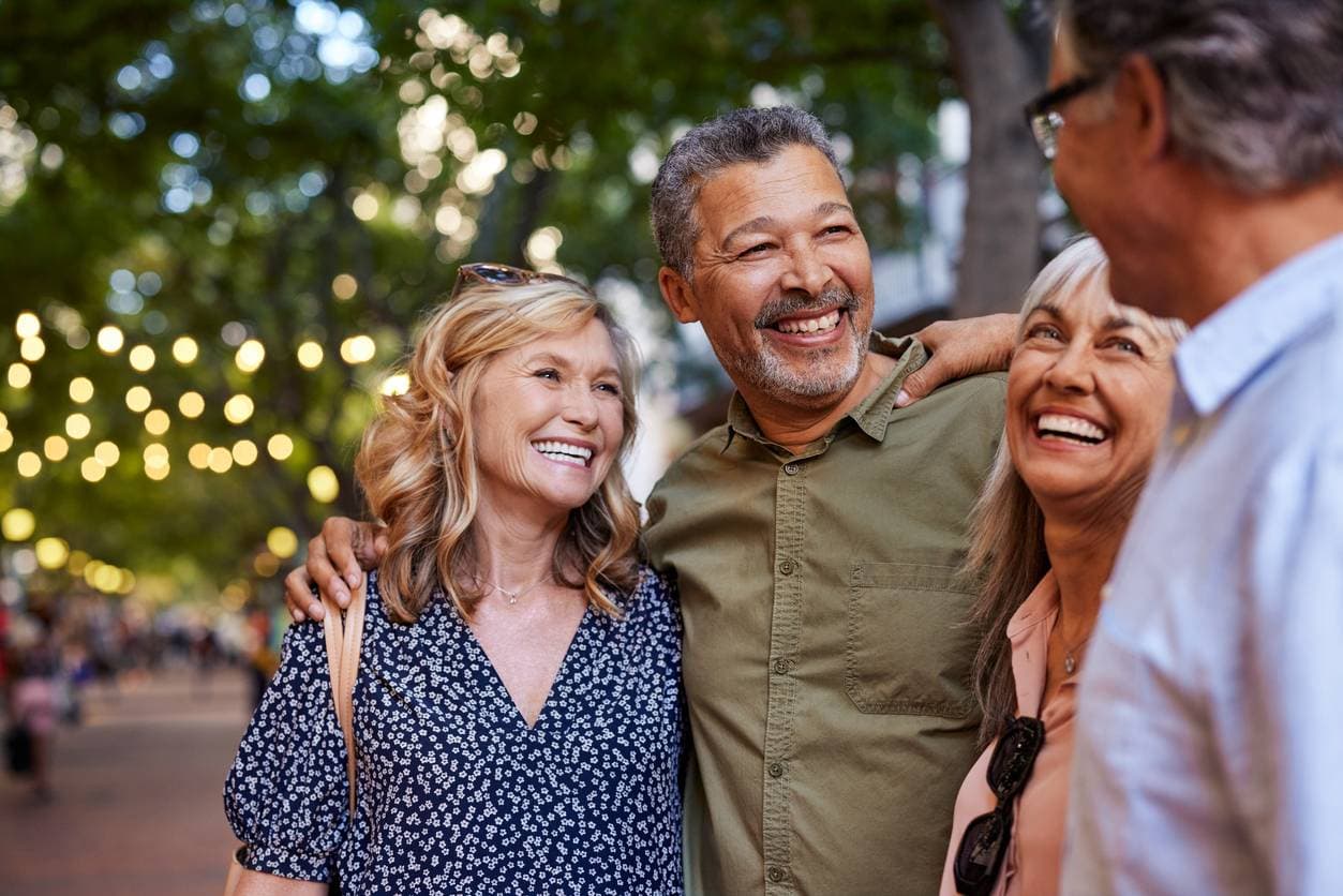 A group of middle-aged people smile and look at each other on a walkable street at dusk