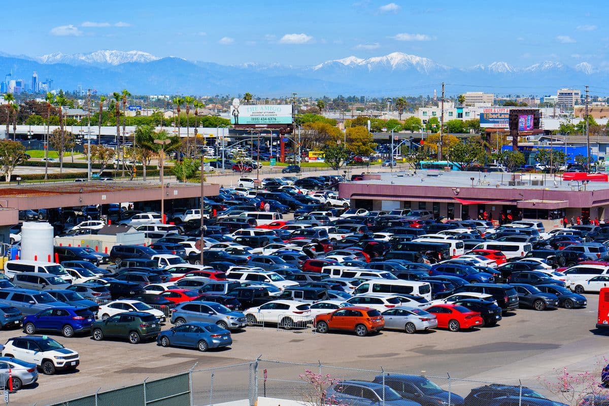 Car rental lot near Los Angeles International Airport, with rows of vehicles and snow-capped mountains in the background.