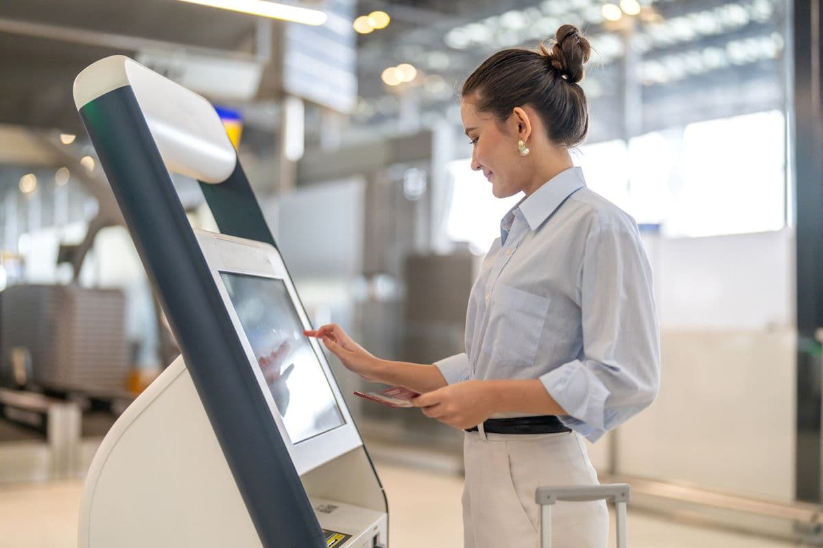 Traveler taps an airport check-in kiosk screen before dropping off her checked bag