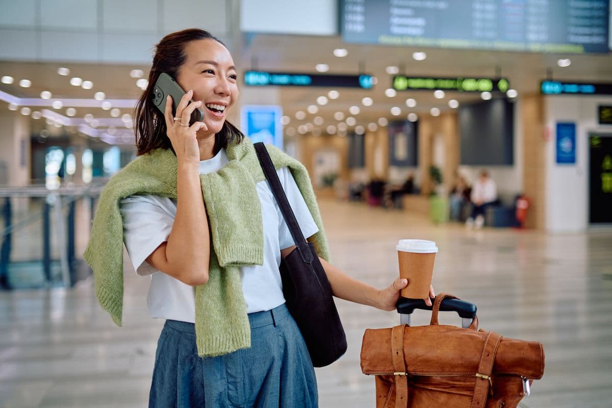 A woman in an airport with a suitcase talking on her phone