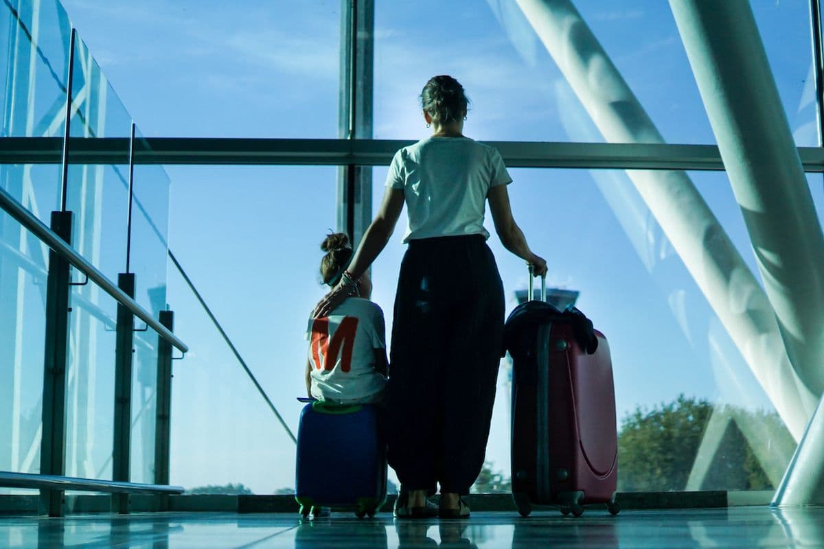 Parent and child with suitcases at an airport terminal window