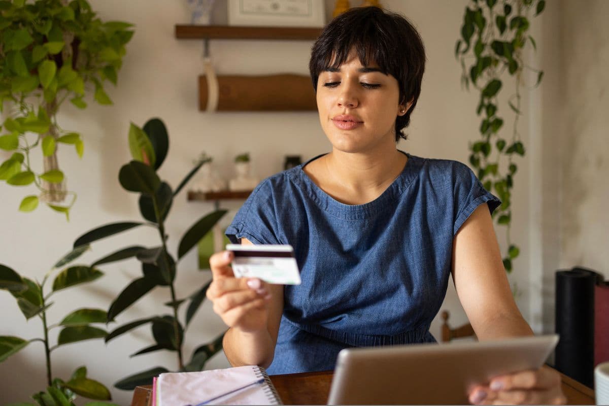Woman sitting at a desk holding a credit card while looking at a laptop.