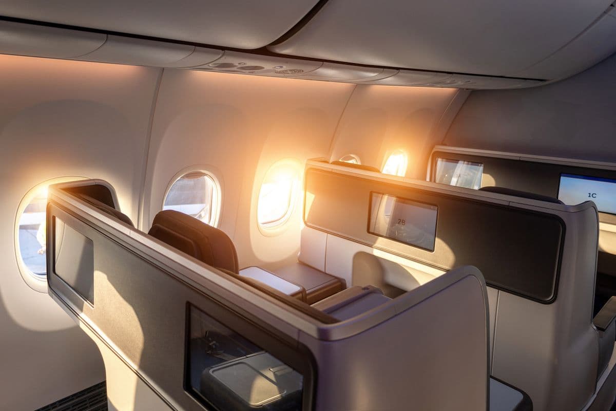 A modern business-class cabin with lie-flat seats arranged along the windows on a wide-body aircraft.