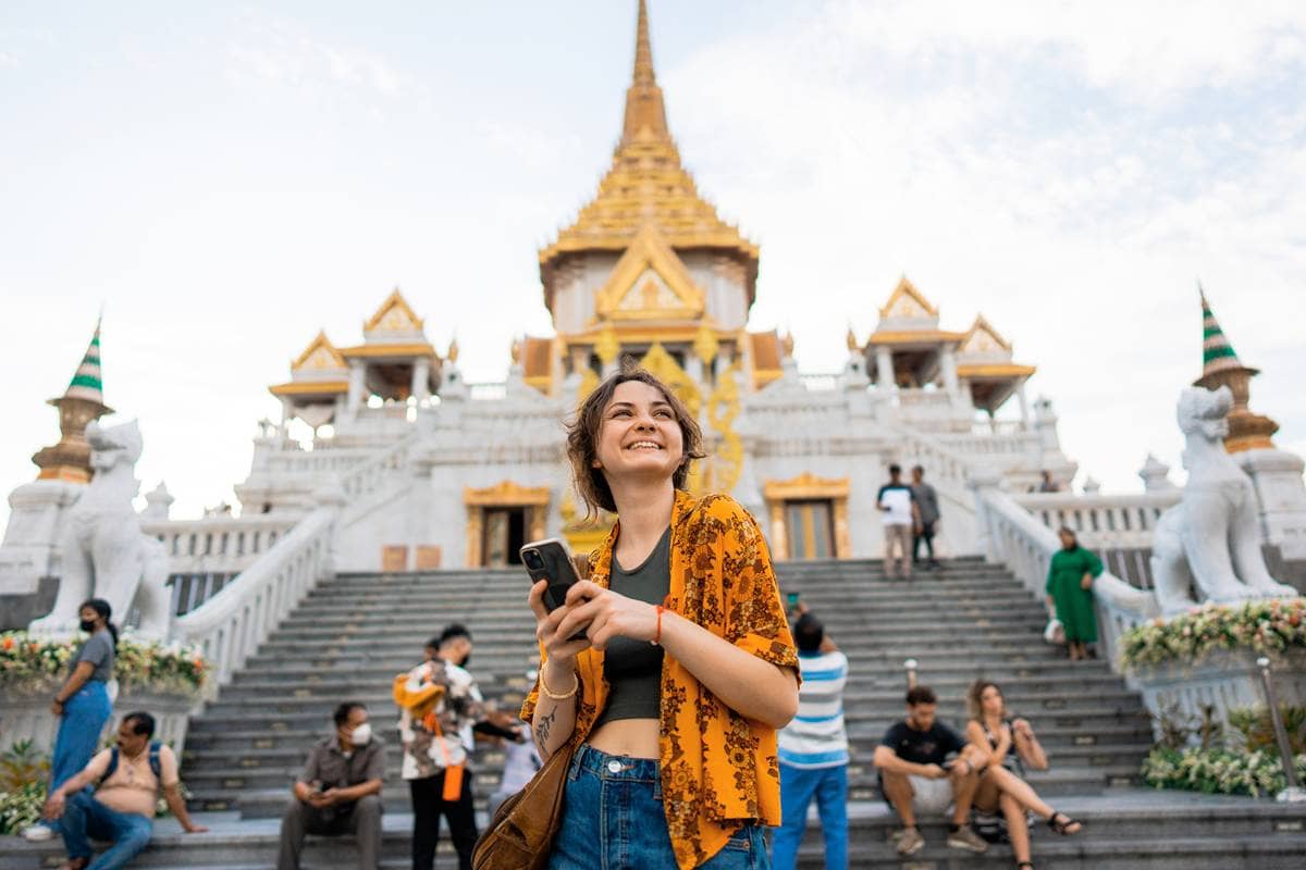 Smiling traveler with phone in front of a golden-spired temple in Bangkok.