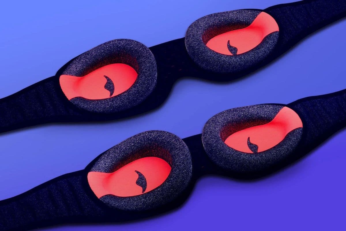 Close-up product image of two Manta Pro sleep masks arranged diagonally on a blue background, showing deep, contoured eye cups with coral-colored interiors designed to block light.