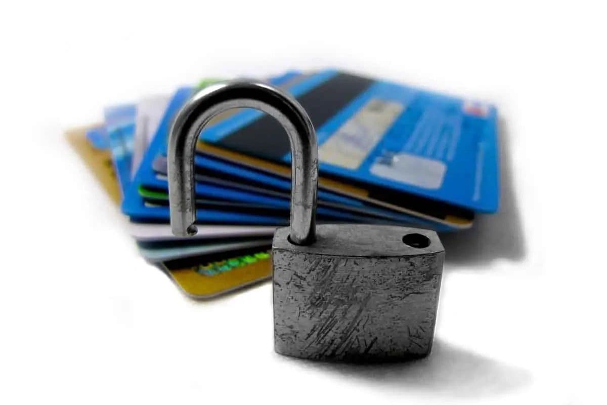 A metal padlock placed in front of a blurred stack of credit cards on a white background.