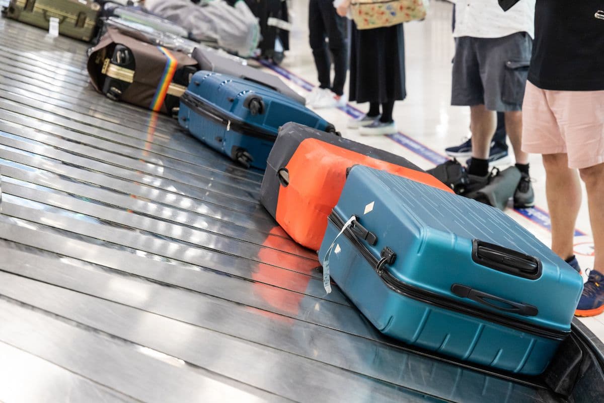 Hard-shell suitcases lined up on an airport baggage carousel as travelers stand alongside waiting to collect their luggage