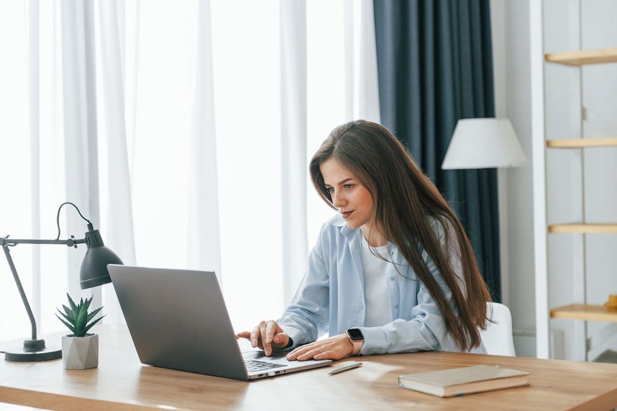 Woman sitting at a desk using a laptop to manage online bill payments at home.